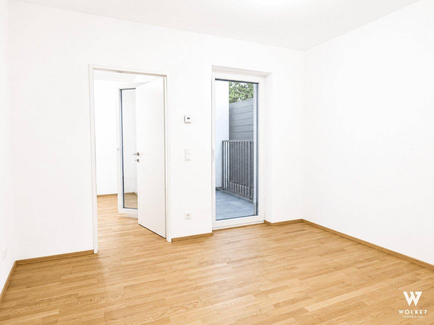 Heller Raum mit Holzboden und Zugang zu einem kleinen Balkon.
