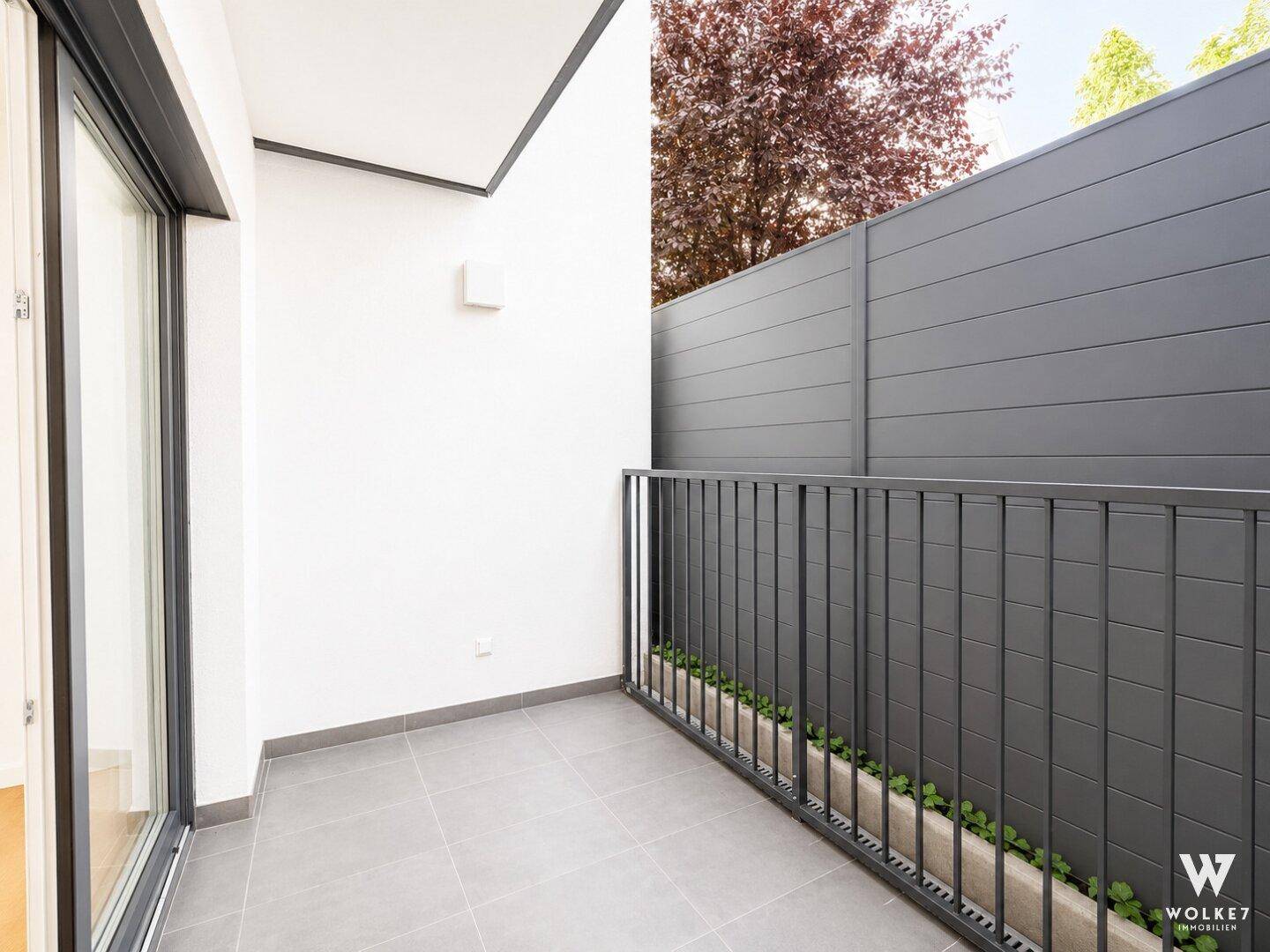 Kleiner Balkon mit grauen Fliesen und Metallgeländer, umgeben von einer Sichtschutzwand.