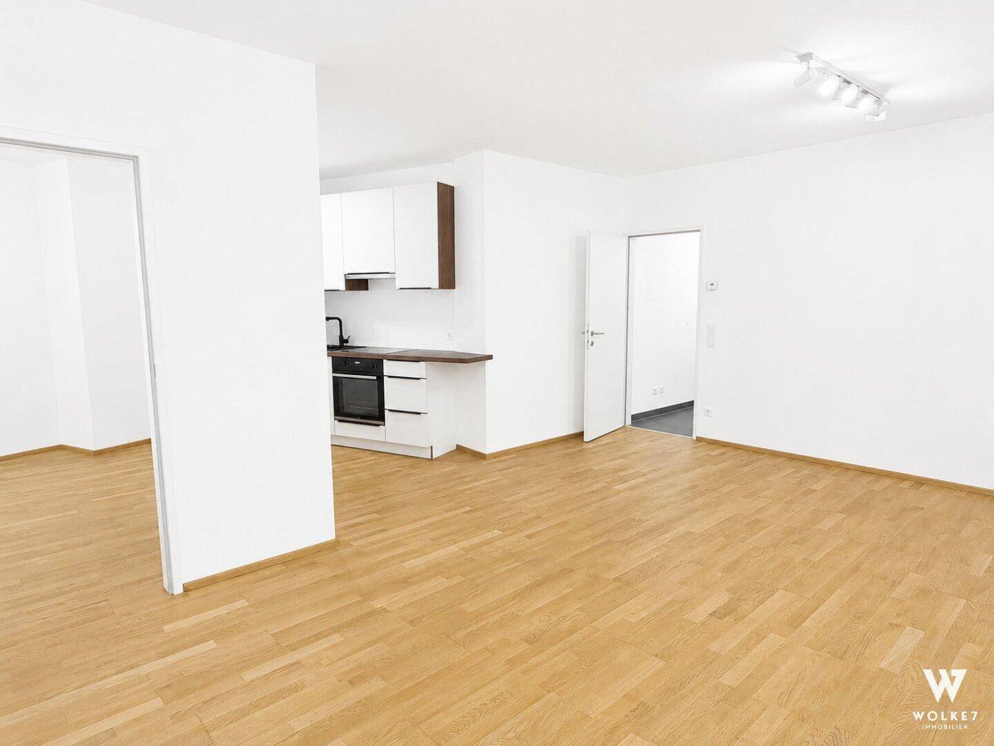 Offener Wohnbereich mit Holzboden und integrierter, moderner Küchenzeile in Weiß.