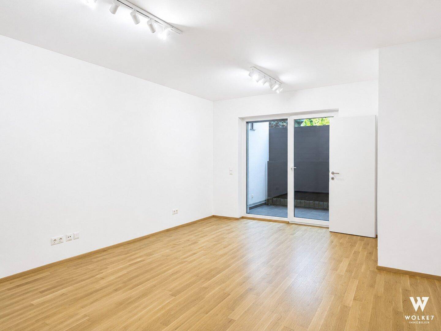 Geräumiger, leerer Raum mit Holzboden und großen Fenstern, die viel Tageslicht hereinlassen.