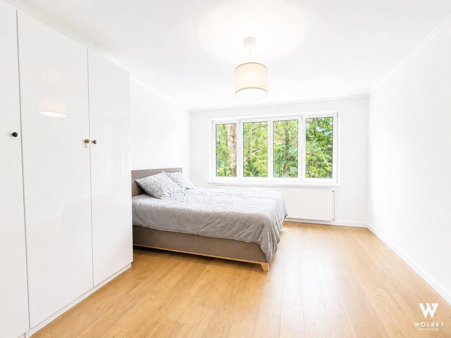 Geräumiges Schlafzimmer mit hellem Holzboden, großen Fenstern und Blick ins Grüne.