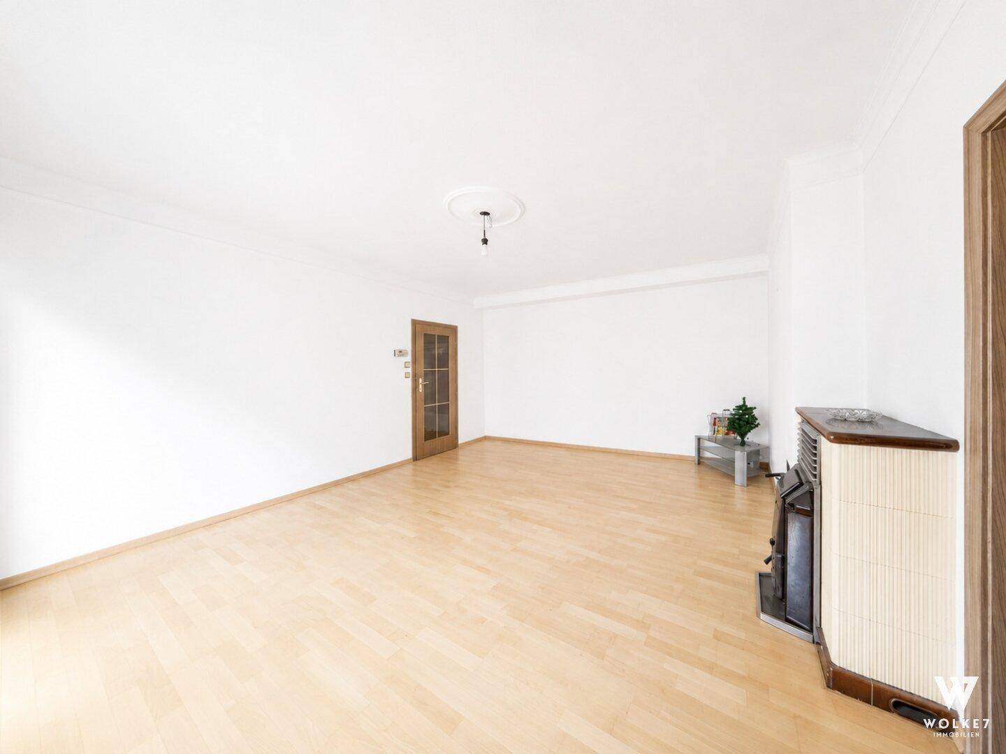 Heller Wohnbereich mit Holztür und einem traditionellen Kachelofen in der Ecke.