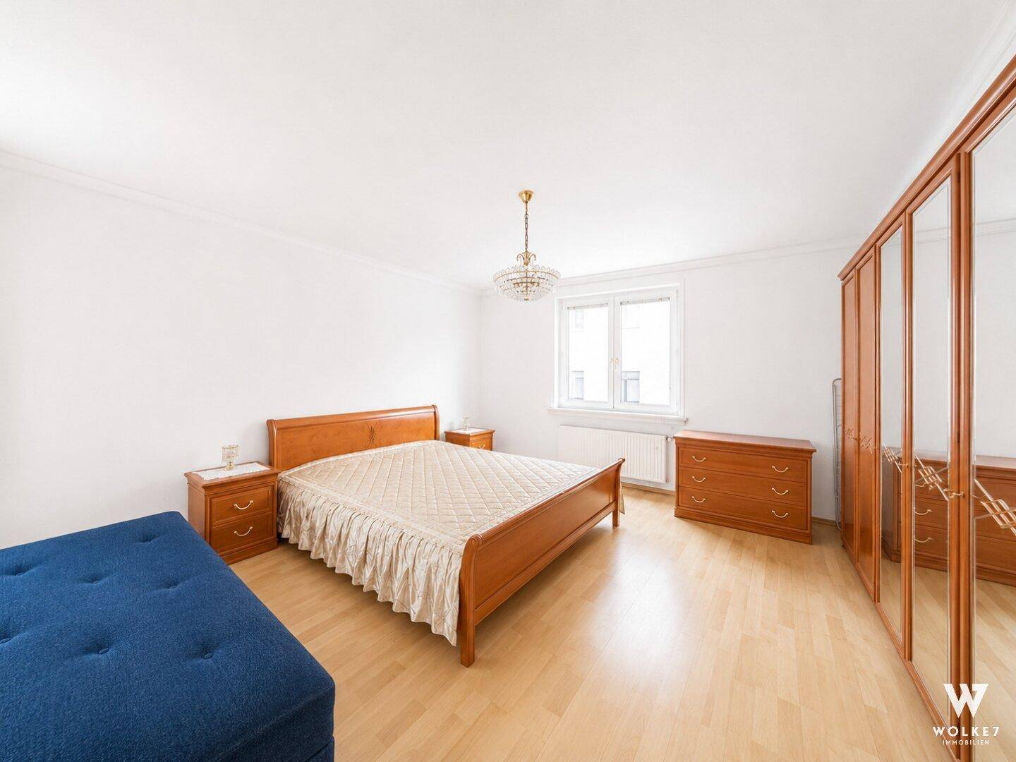 Helles Schlafzimmer mit Holzbett, Nachttischen und einem blauen Polstermöbel.