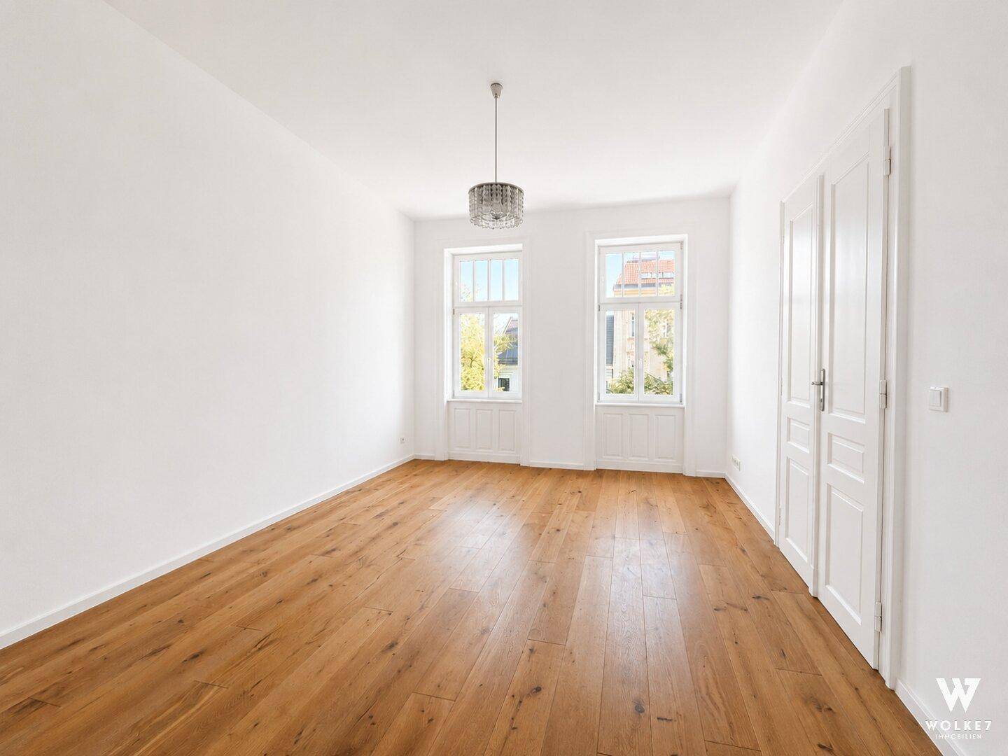 Geräumiger, leerer Raum mit Holzboden, Doppeltüren und einem eleganten Kronleuchter.