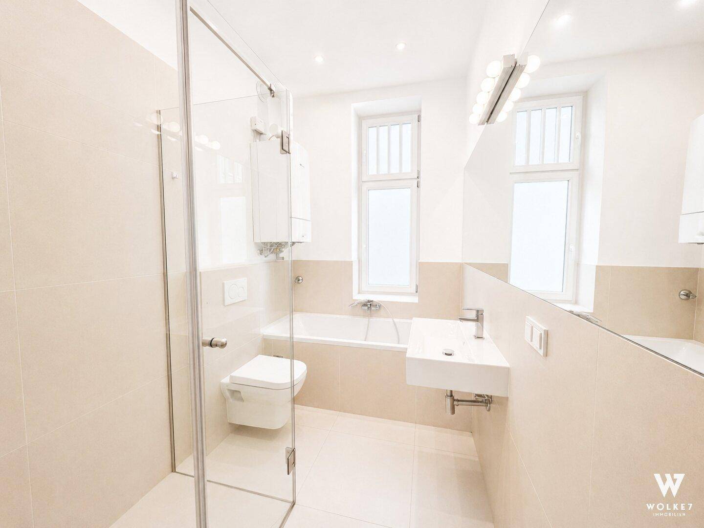 Modernes Badezimmer mit beigefarbenen Fliesen, Badewanne, Dusche und Fenster für Tageslicht.