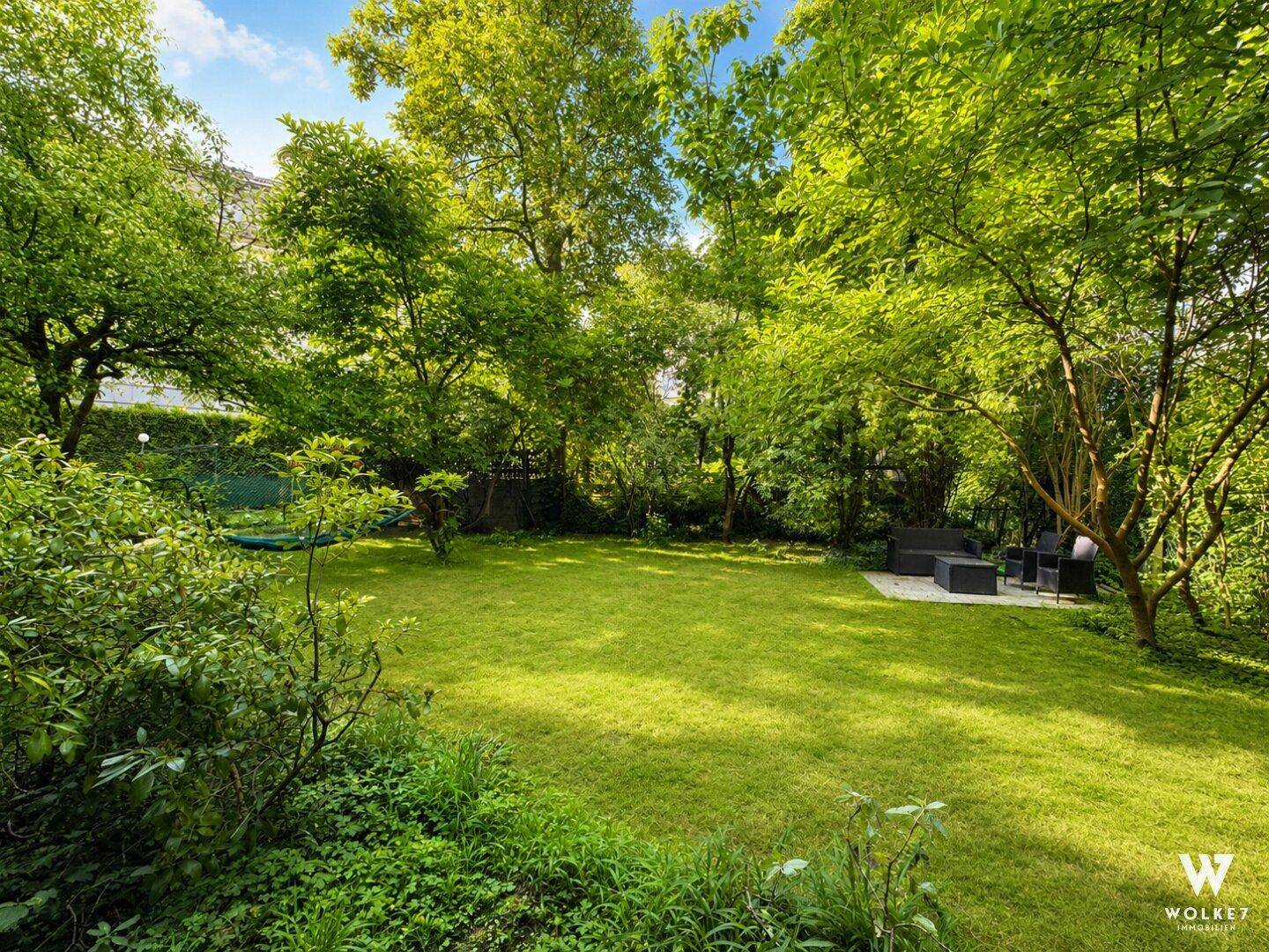 Großer, gepflegter Garten mit Rasenfläche, alten Bäumen und einer gemütlichen Sitzecke.