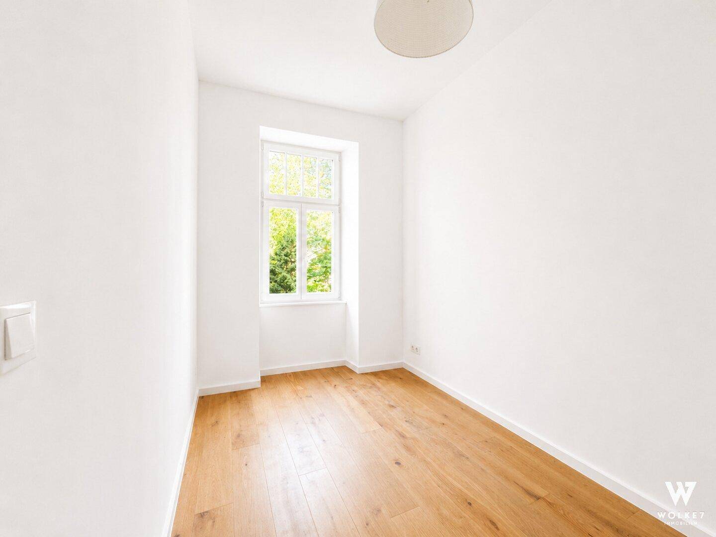 Kleiner, heller Raum mit Holzboden und einem Fenster mit Blick ins Grüne.