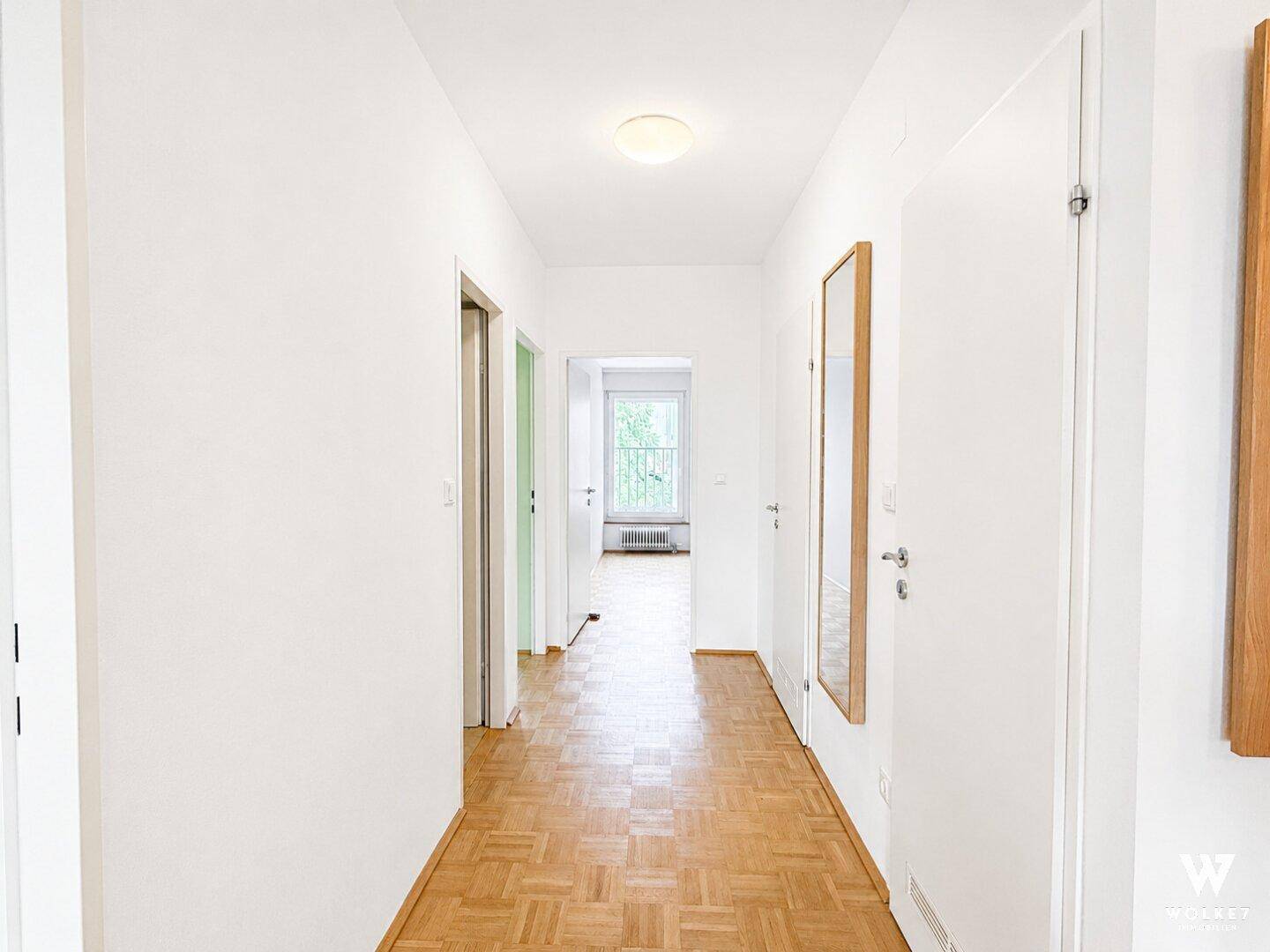 Heller Flur mit Parkettboden, weißen Wänden und Türen zu den angrenzenden Zimmern.