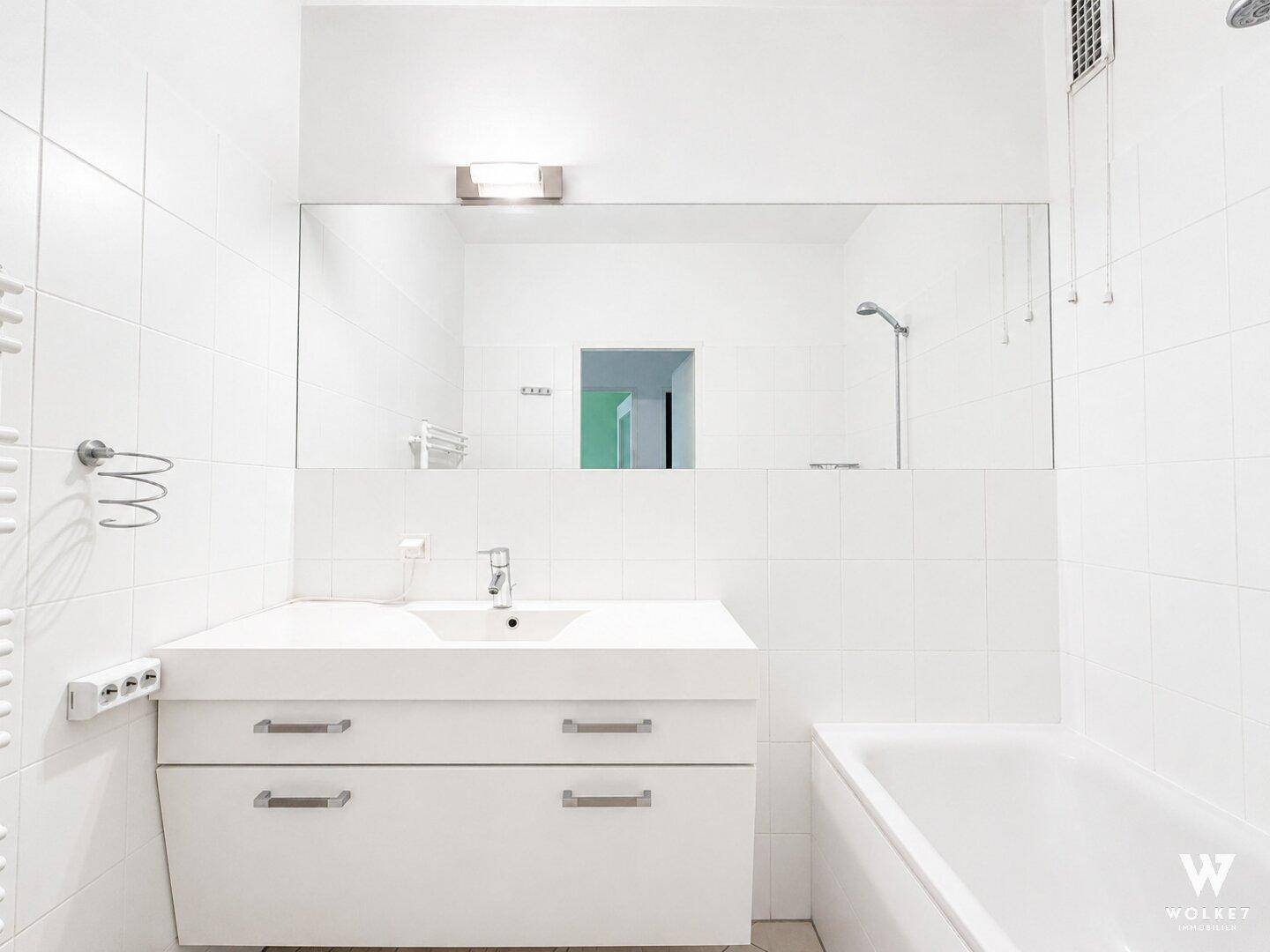 Modernes Badezimmer ganz in Weiß mit Badewanne, Dusche und großem Spiegel über dem Waschbecken.
