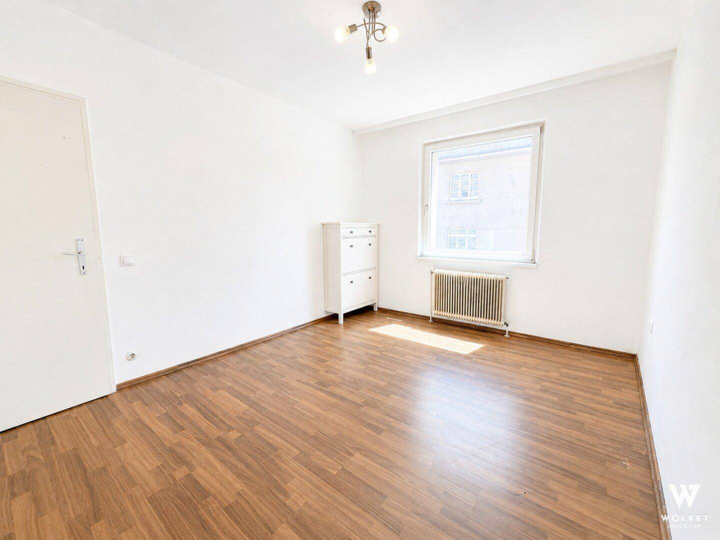 Leeres Schlafzimmer mit Laminatboden, weißen Wänden und einem Fenster für natürliches Licht.