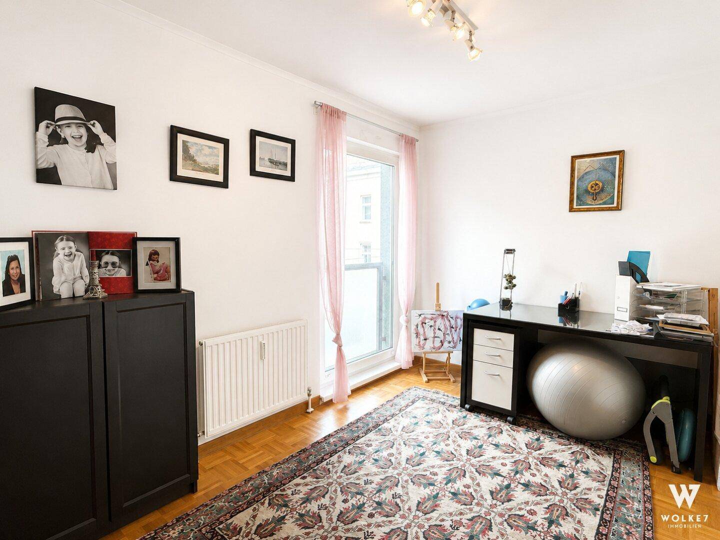 Arbeitszimmer mit Schreibtisch, Parkettboden und Zugang zu einem Balkon.