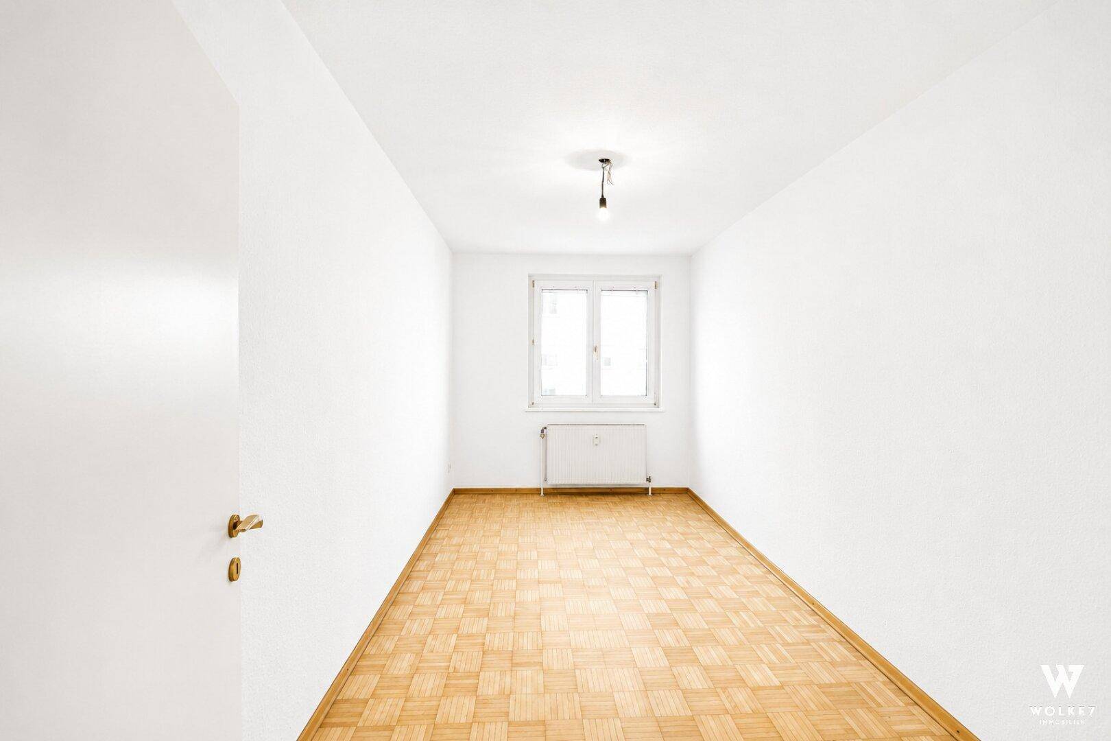 Heller, leerer Raum mit Parkettboden und einem Fenster, ideal als Schlaf- oder Arbeitszimmer.
