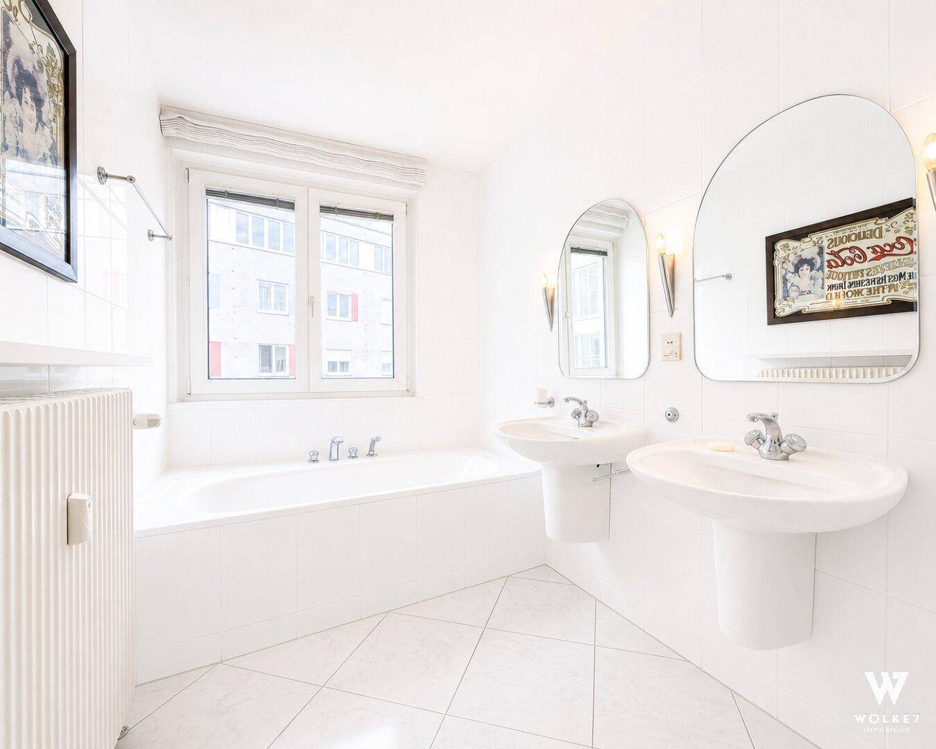 Helles Badezimmer mit zwei Waschbecken, Badewanne und großem Fenster.