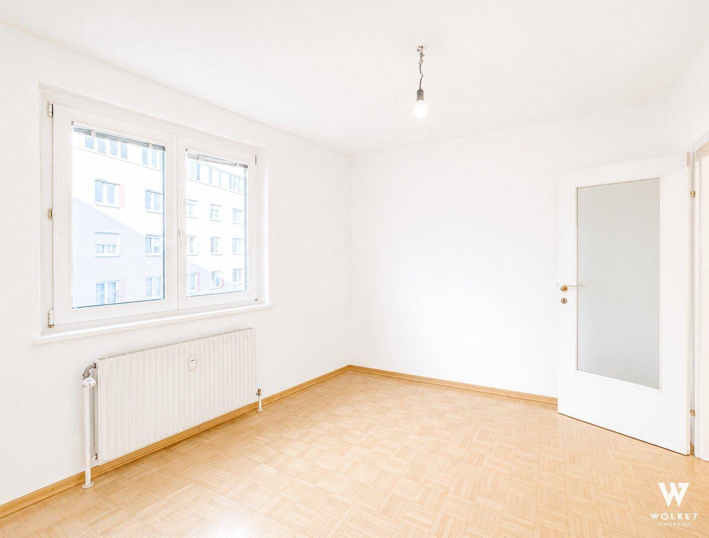 Heller, leerer Raum mit Parkettboden und einer Tür mit Glaseinsatz.