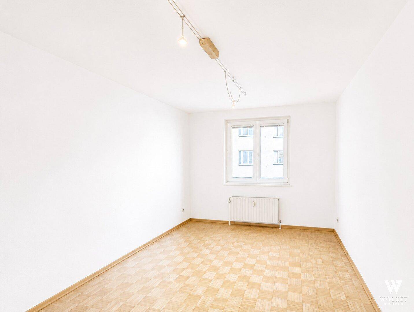 Leeres Zimmer mit Parkettboden und Fenster, ideal für ein Schlaf- oder Gästezimmer.