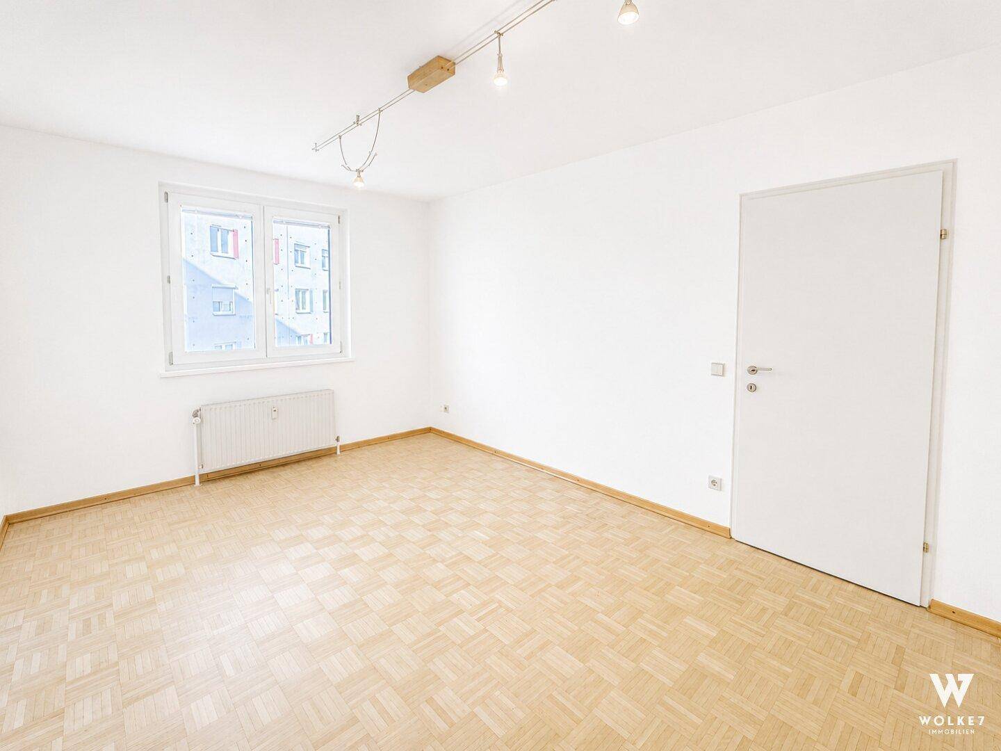Leeres Zimmer mit Parkettboden und Fenster, bereit für individuelle Gestaltung.