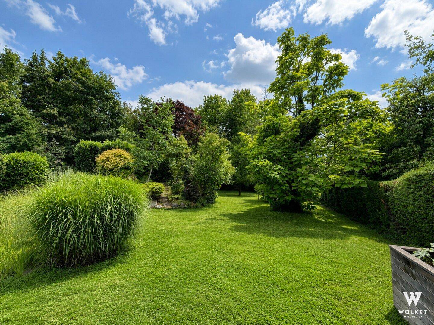 Großer, gepflegter Garten mit weitläufiger Rasenfläche, Bäumen und Ziergräsern.