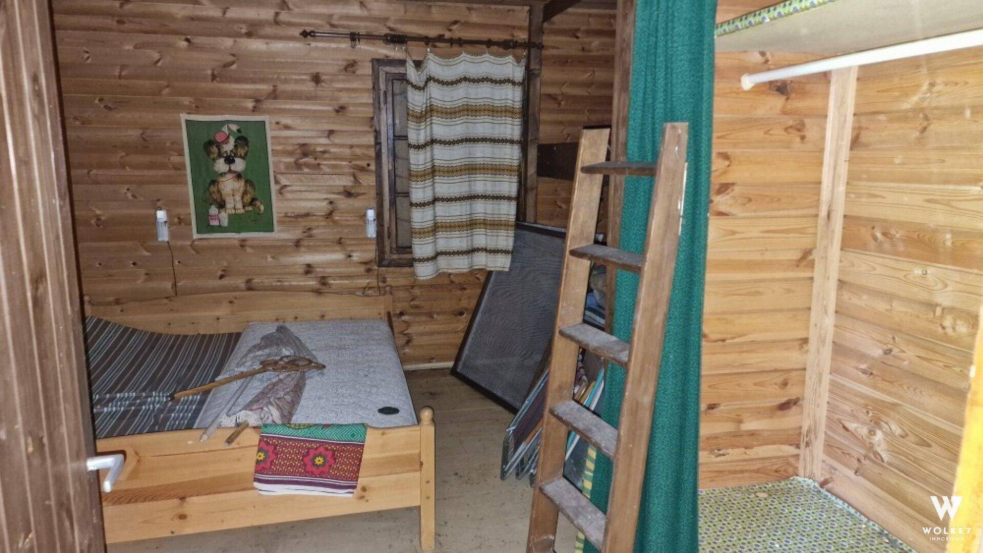 Einfaches Schlafzimmer in einer Holzhütte mit Holzwänden, einem Bett und einer Leiter zu einem Hochbett.