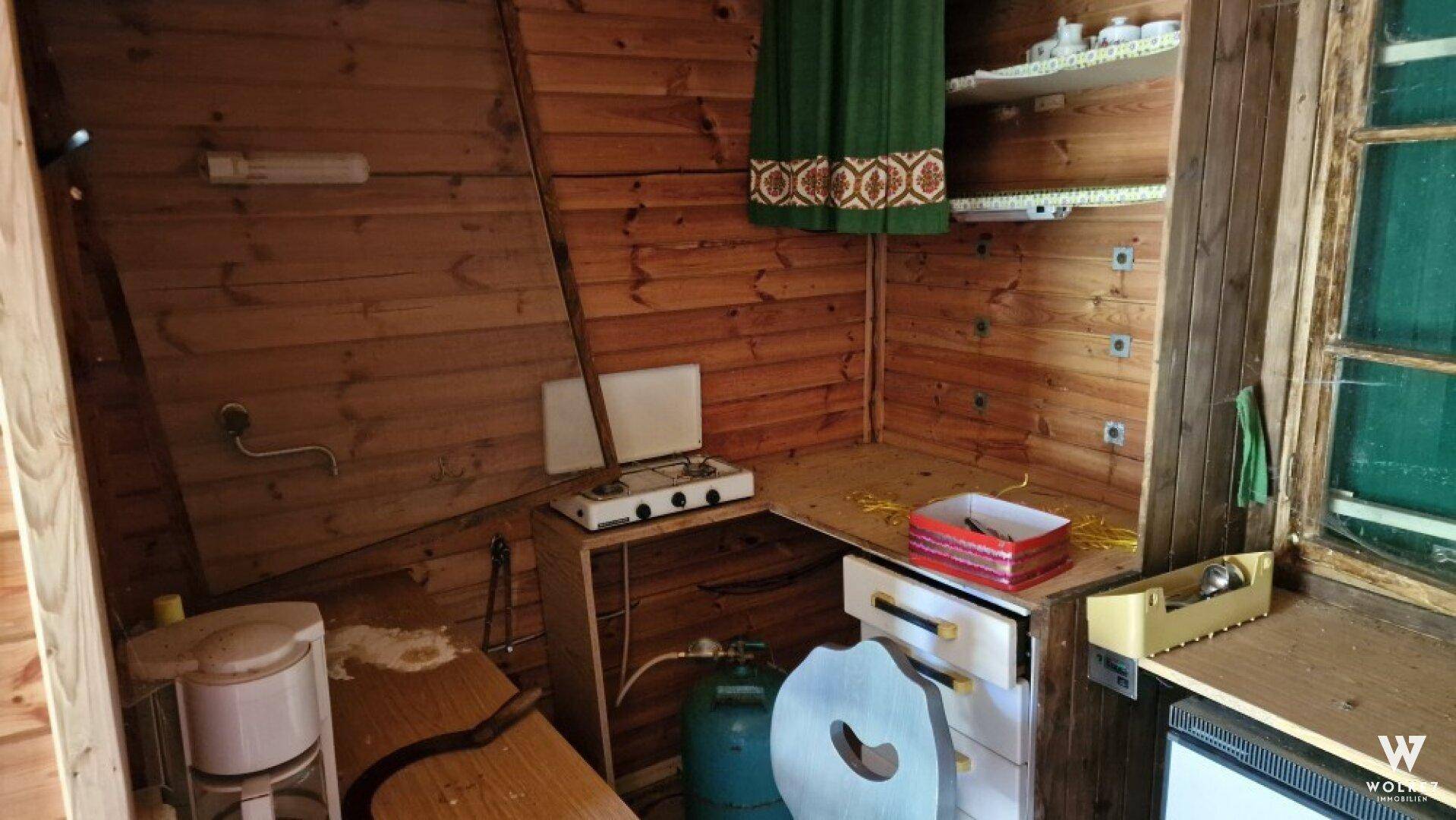 Kleine Küchenzeile in einer Holzhütte mit Gaskocher, einfachen Regalen und einem Fenster.