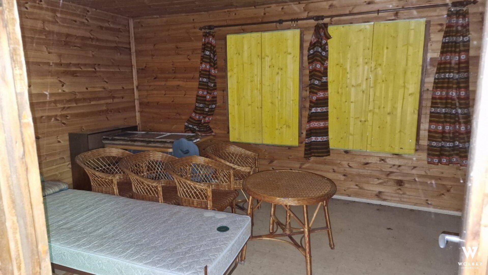 Gemütlicher Wohnbereich in einer Holzhütte mit Holzwänden, Korbmöbeln und einem Schlafplatz.