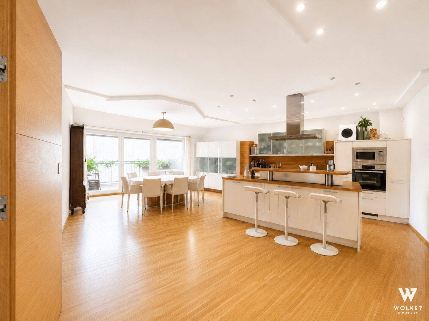 Heller offener Wohn- und Essbereich mit moderner Küche, Holzboden und Zugang zum Balkon.
