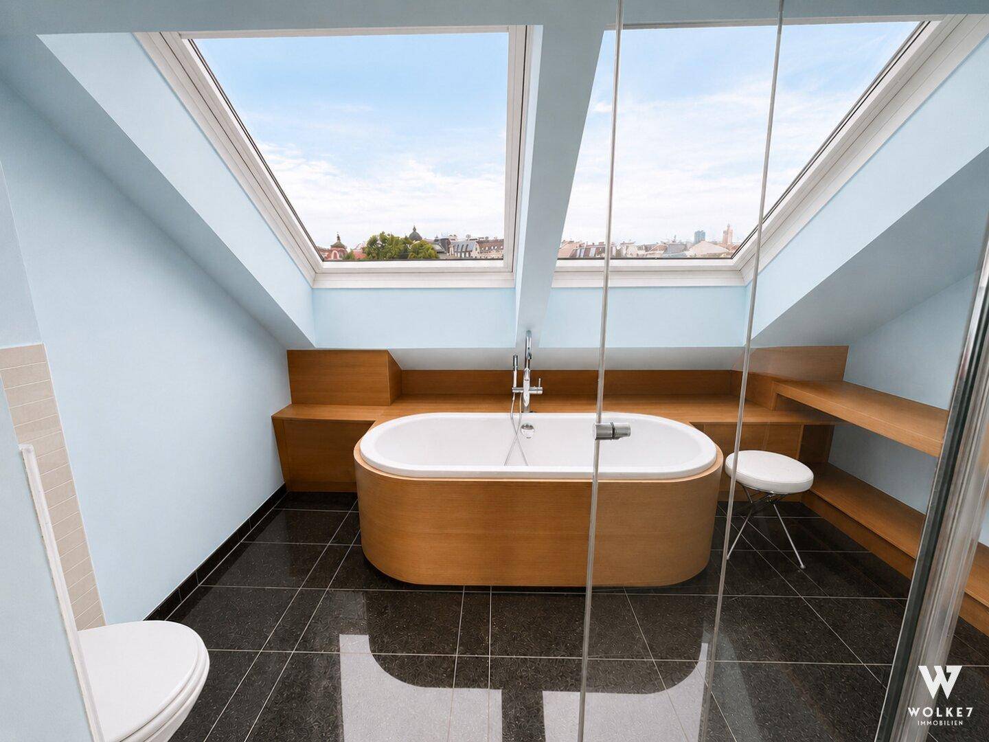Luxuriöses Dachgeschoss-Badezimmer mit freistehender Badewanne unter großen Dachfenstern.