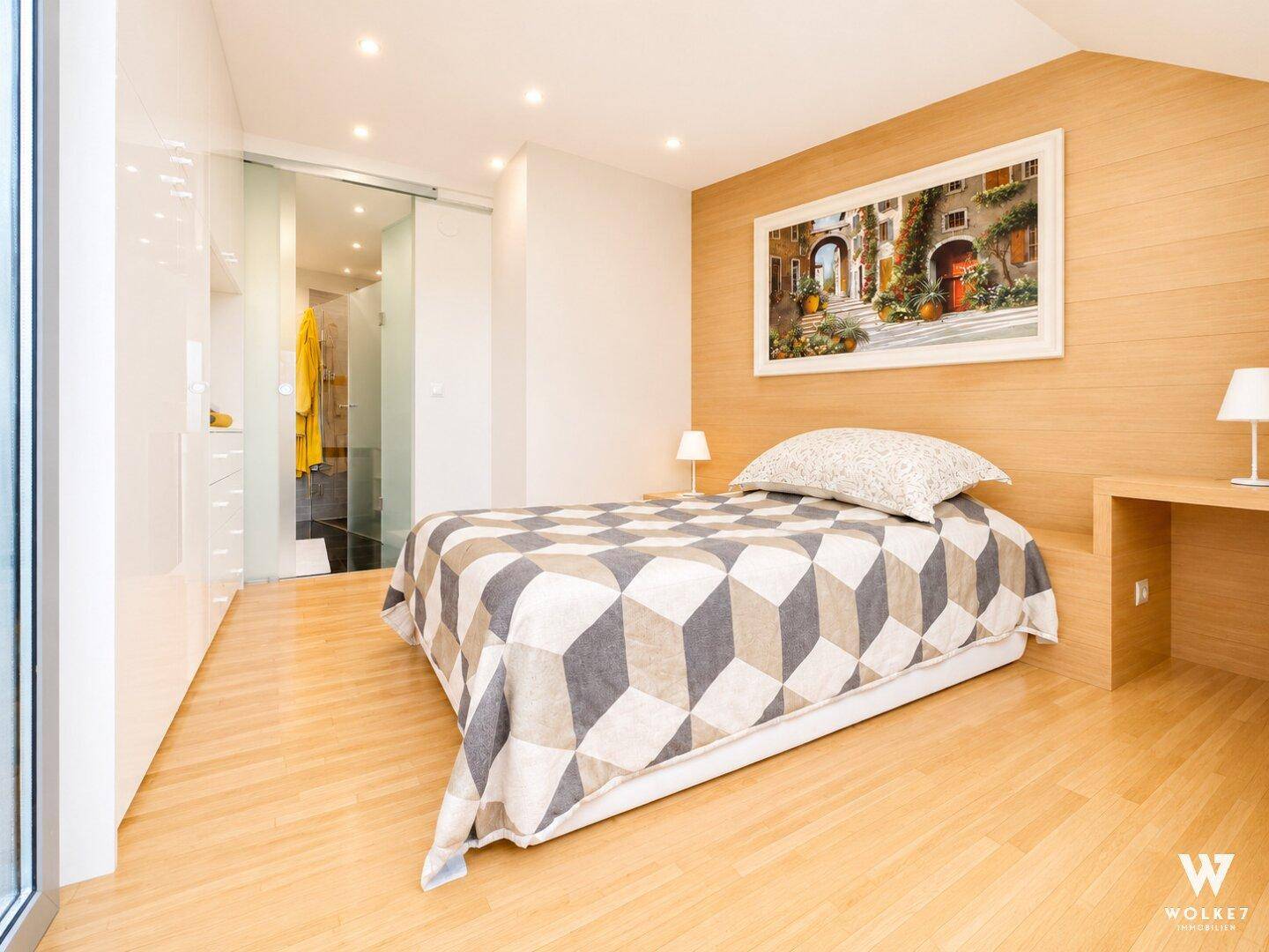 Schlafzimmer mit Holzboden, modernem Bett und Glasschiebetür zum angrenzenden Badezimmer.