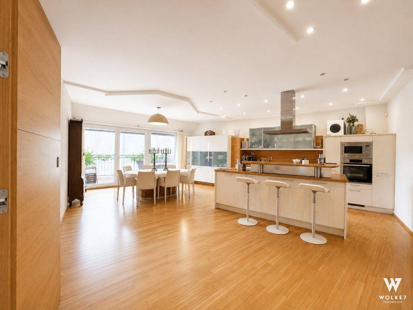Heller offener Wohn- und Essbereich mit moderner Küche, Holzboden und Zugang zum Balkon.