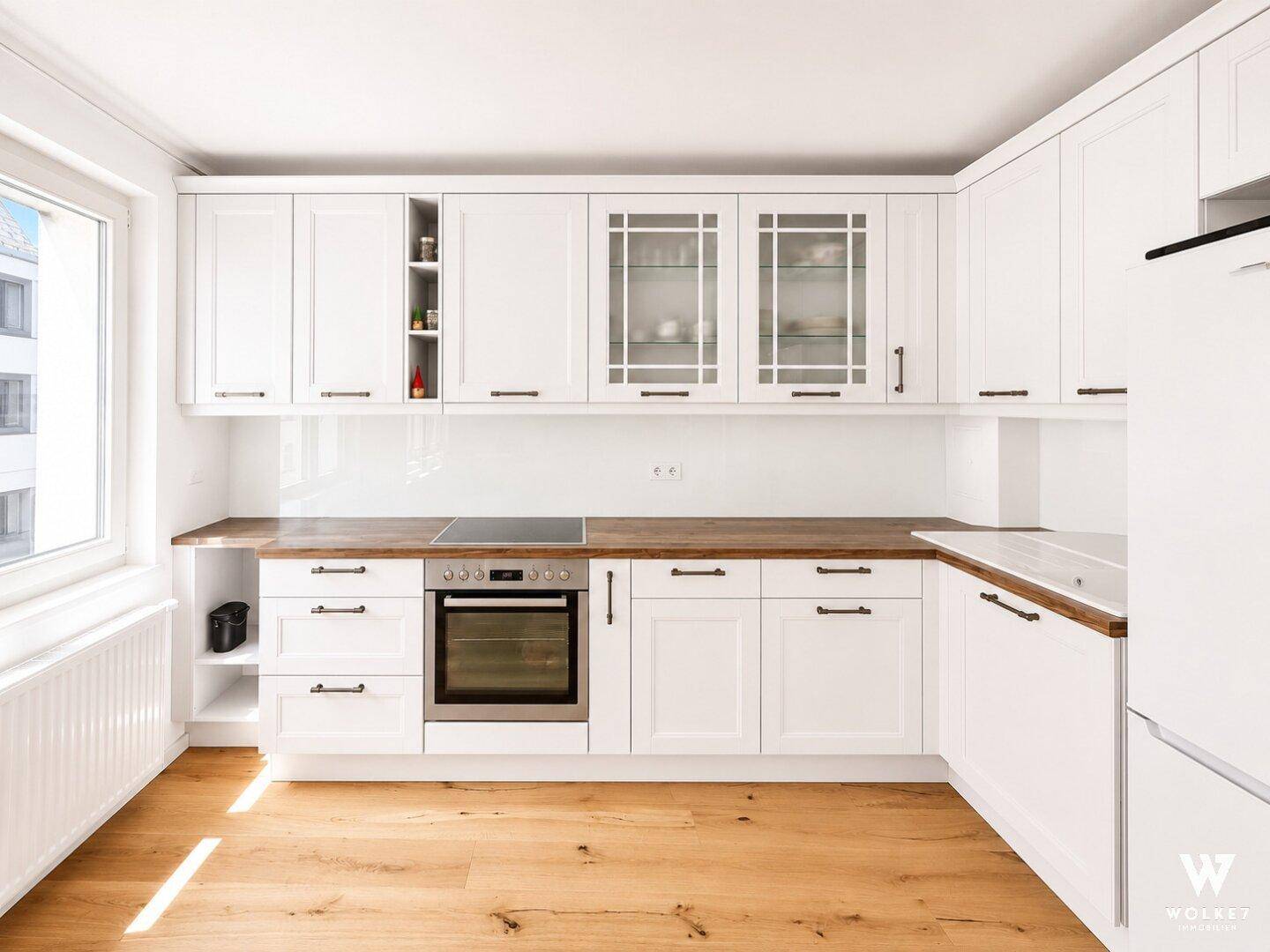 Moderne weiße Einbauküche mit Holz-Arbeitsplatten, Induktionskochfeld und integriertem Backofen.