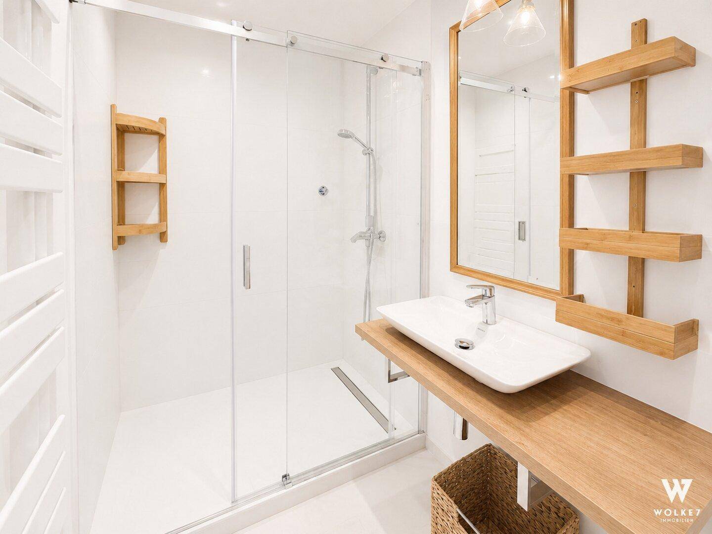 Zeitgemäßes Badezimmer mit geräumiger Duschkabine, Holzwaschtisch und weißen Fliesen.