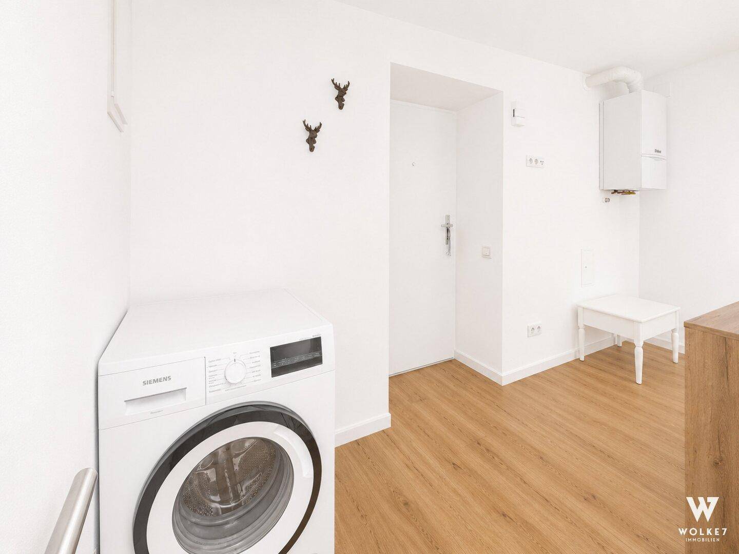 Hauswirtschaftsraum mit Waschmaschine, Warmwasserbereiter und Zugang zur Wohnung.