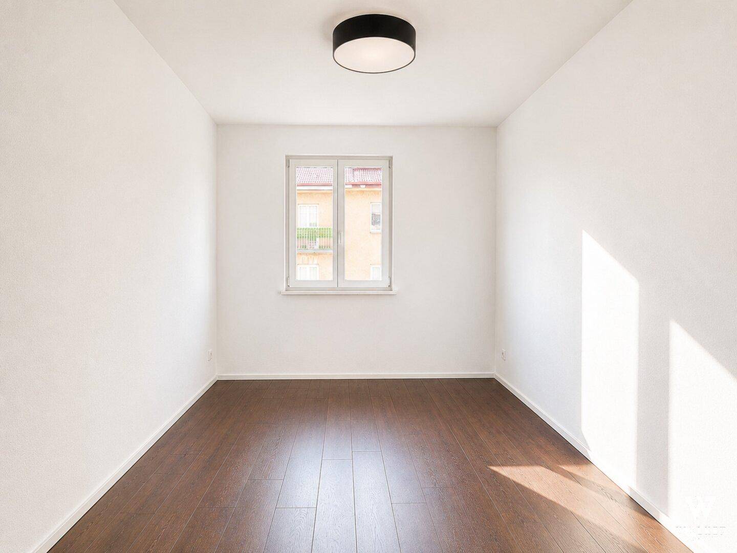 Heller, unmöblierter Raum mit dunklem Holzboden, der von der Sonne durchflutet wird.