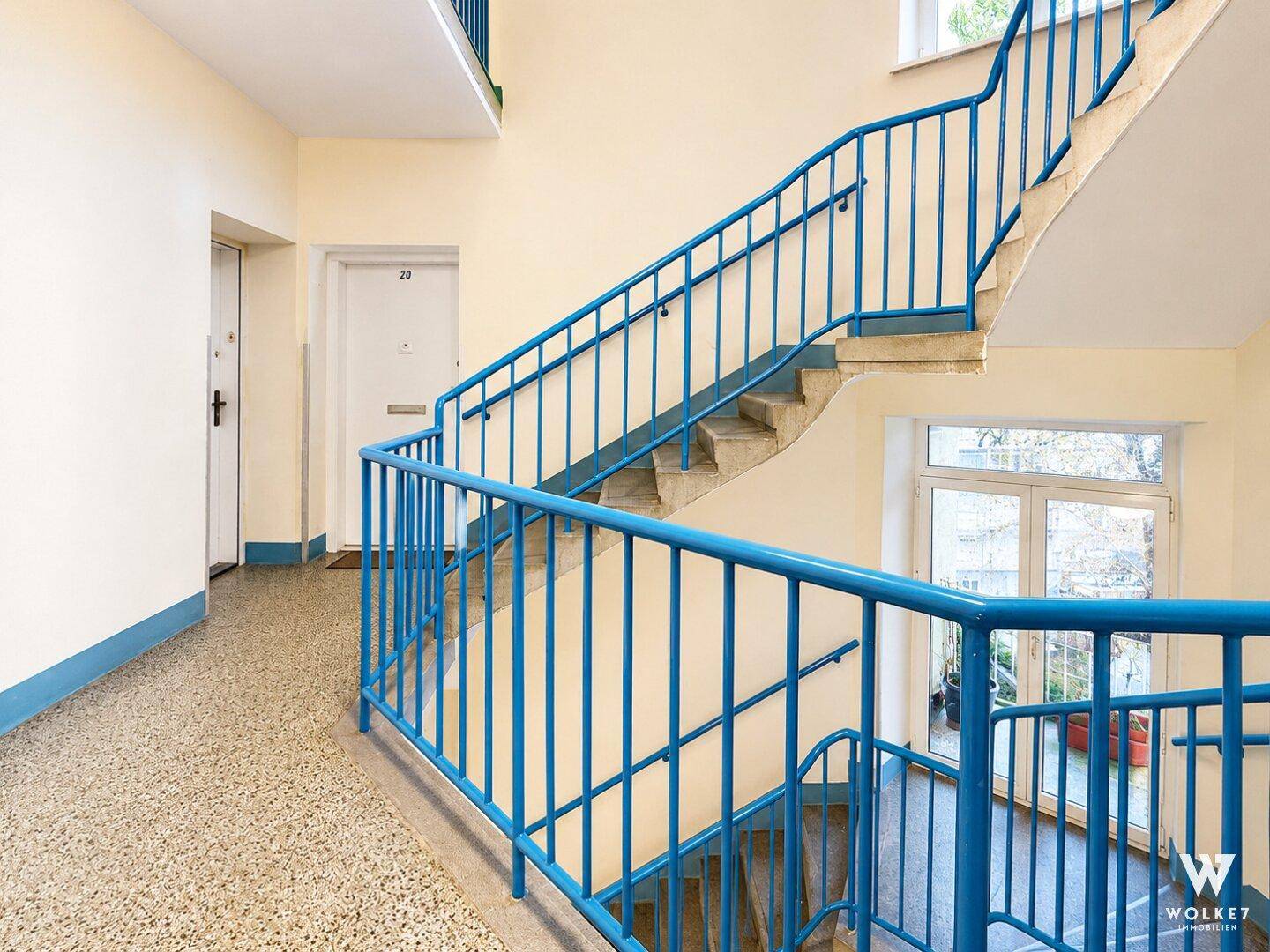 Treppenhaus mit blauen Geländern und Terrazzoboden in einem Mehrfamilienhaus.