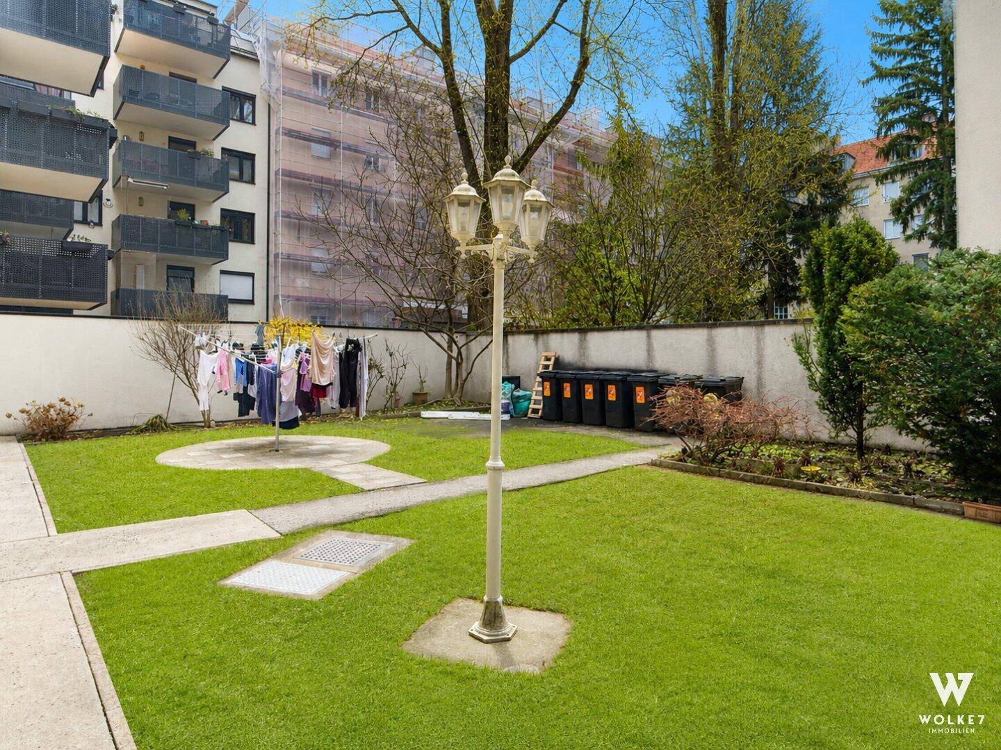 Gepflegter Gemeinschaftsgarten mit Rasenfläche, Wäscheleine und Mülltonnen im Hintergrund.