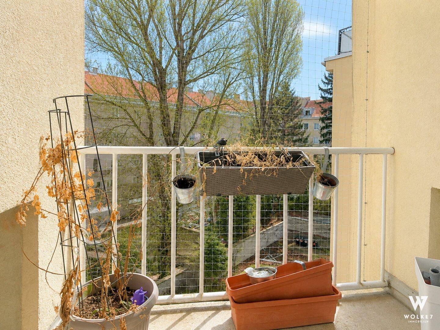 Kleiner Balkon mit Blick auf Bäume und umliegende Gebäude, ausgestattet mit einem Schutznetz.