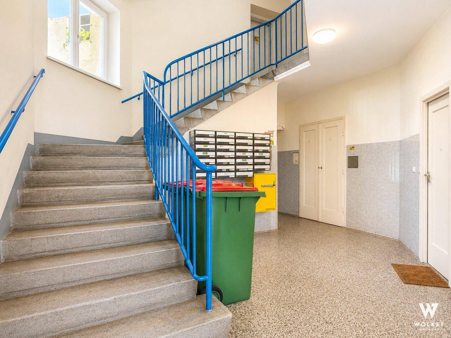 Eingangsbereich mit Treppenhaus, Briefkästen und einem Mülleimer im Gemeinschaftsbereich.