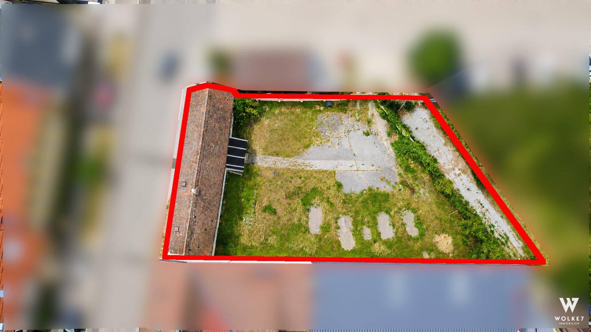 Luftaufnahme eines Grundstücks mit Bestandsgebäude und ungenutzter Freifläche, rot umrandet.
