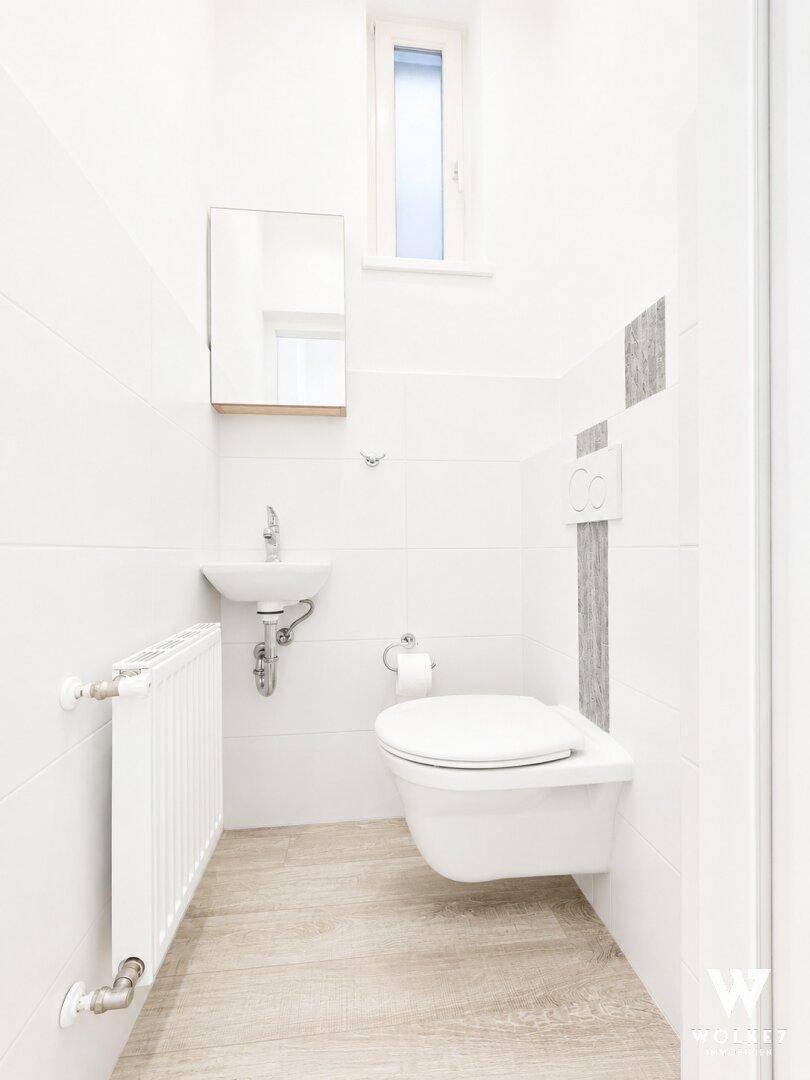 Modernes Gäste-WC mit wandhängender Toilette, kleinem Waschbecken und Heizkörper.