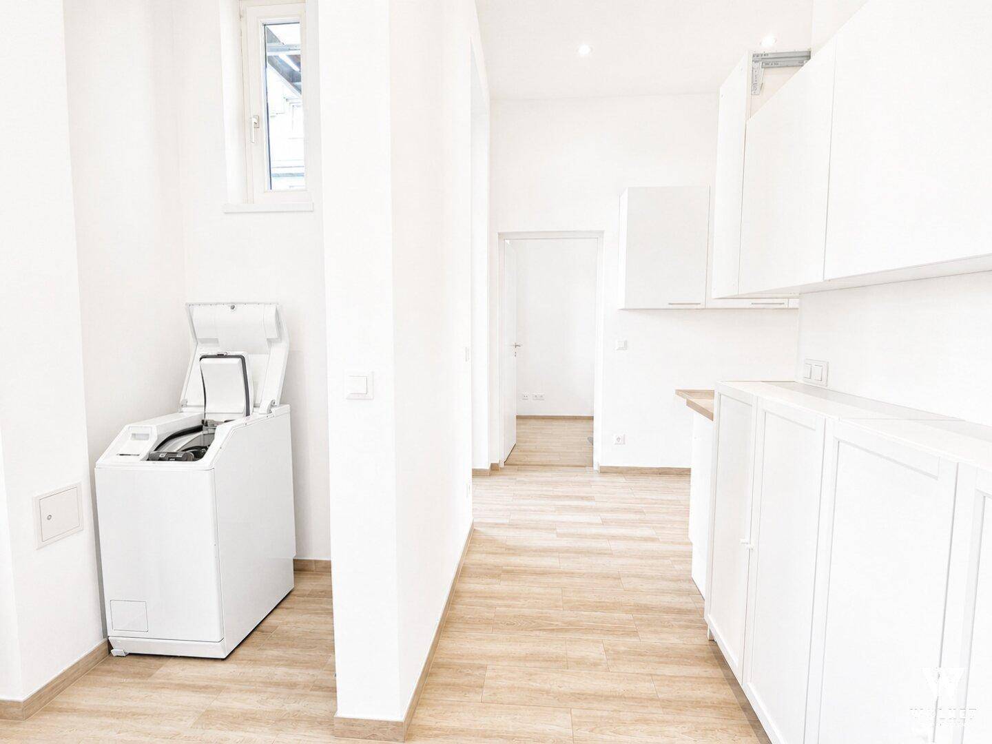 Heller Hauswirtschaftsraum mit Waschmaschine, weißen Schränken und praktischem Holzboden.