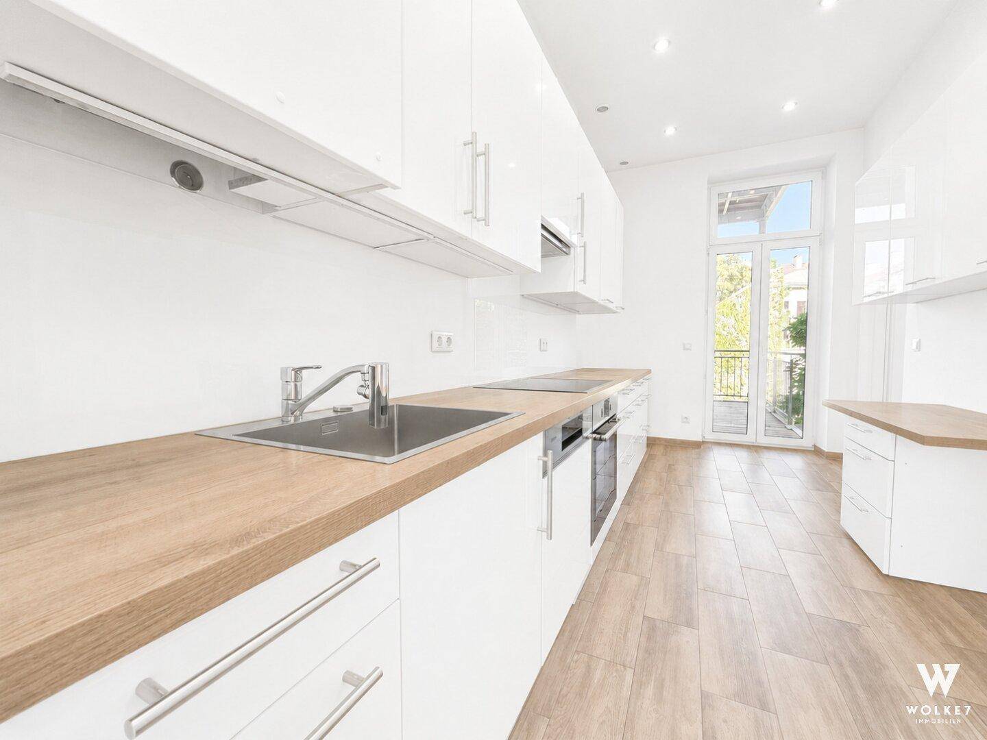 Moderne Küche mit weißen Schränken, Holzarbeitsplatten und Zugang zu einem französischen Balkon.