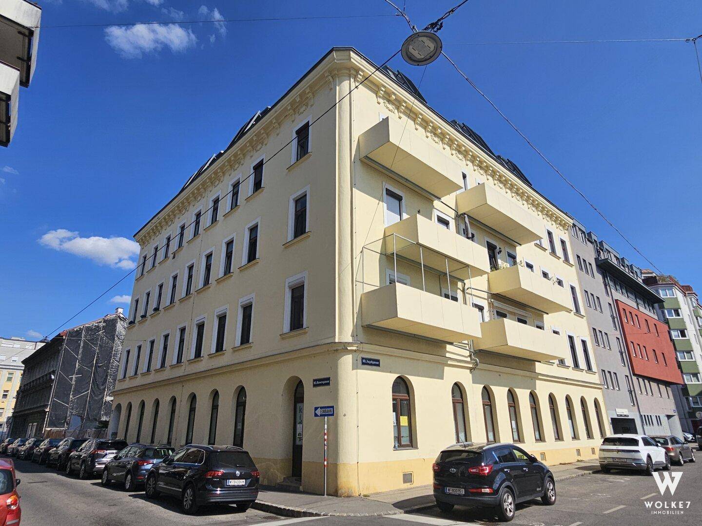 Historisches Eckgebäude mit gelber Fassade, mehreren Balkonen und parkenden Autos auf der Straße.