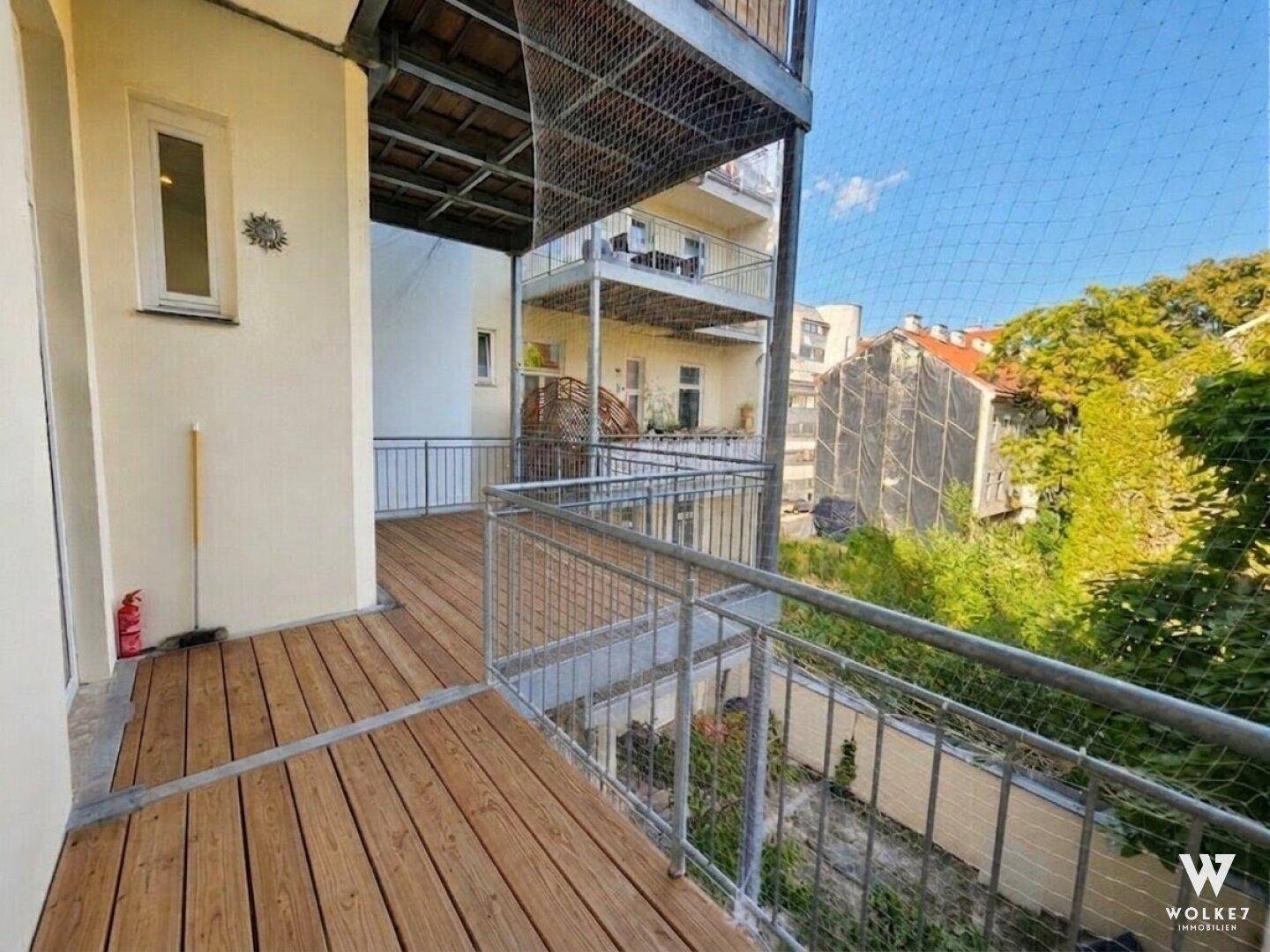 Geräumiger Balkon mit Holzfußboden und Metallgeländer, bietet Blick auf den Innenhof und umliegende Gebäude.