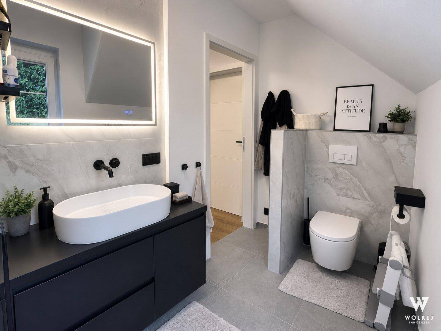 Modernes Badezimmer mit großem beleuchtetem Spiegel, Waschtisch und Wand-WC.