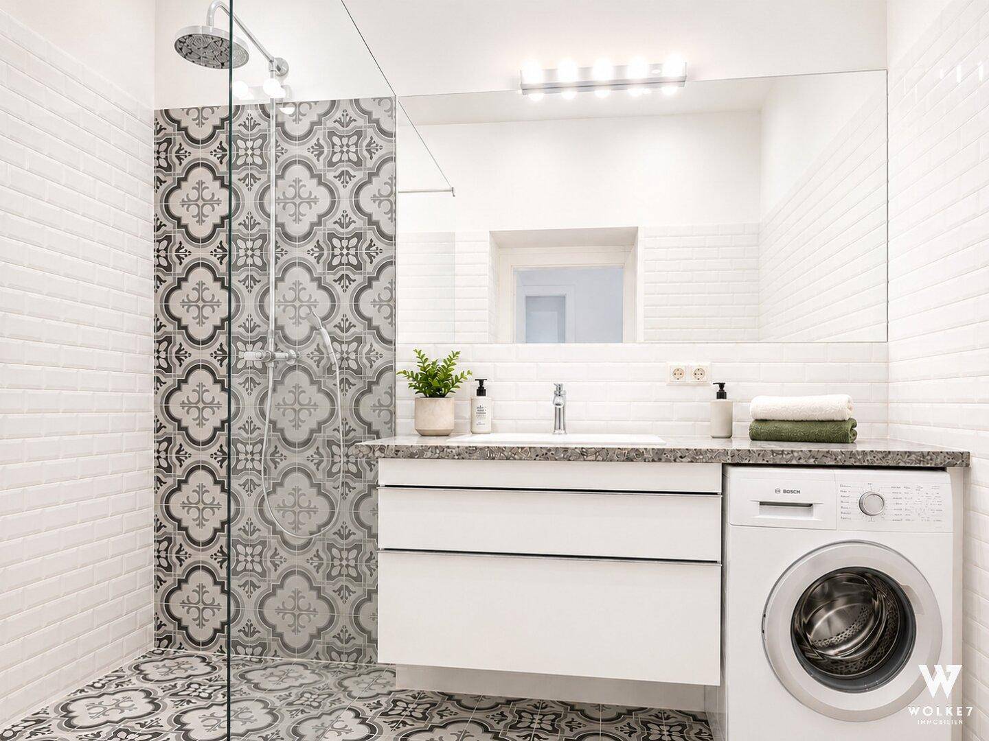Modernes Badezimmer mit begehbarer Dusche, gemusterten Fliesen und integrierter Waschmaschine.