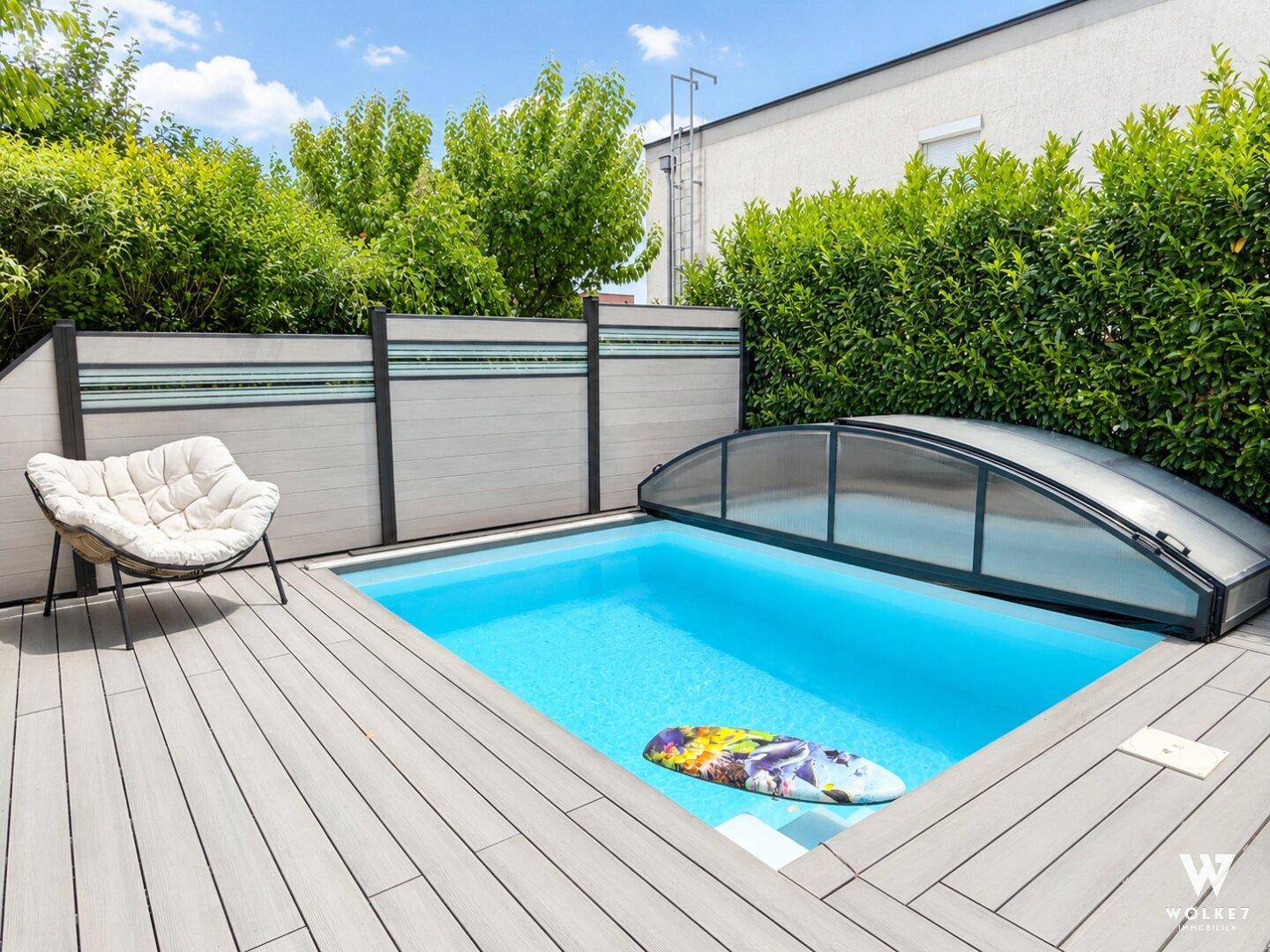 Kleiner Pool mit Holzdeck und Liegestuhl, umgeben von einer grünen Hecke.