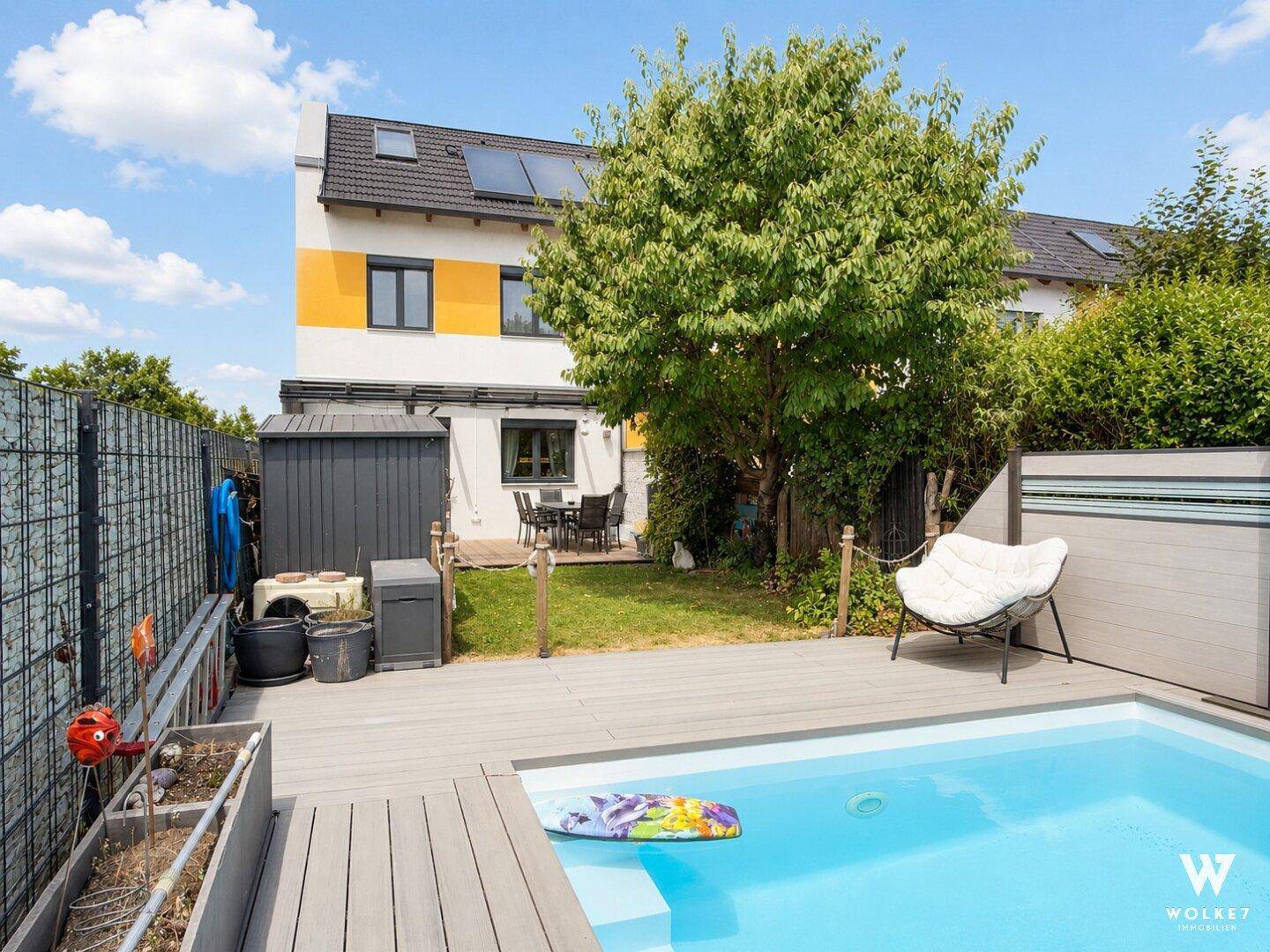 Gartenbereich mit Pool, Holzdeck, Rasenfläche und einer Terrasse im Hintergrund.