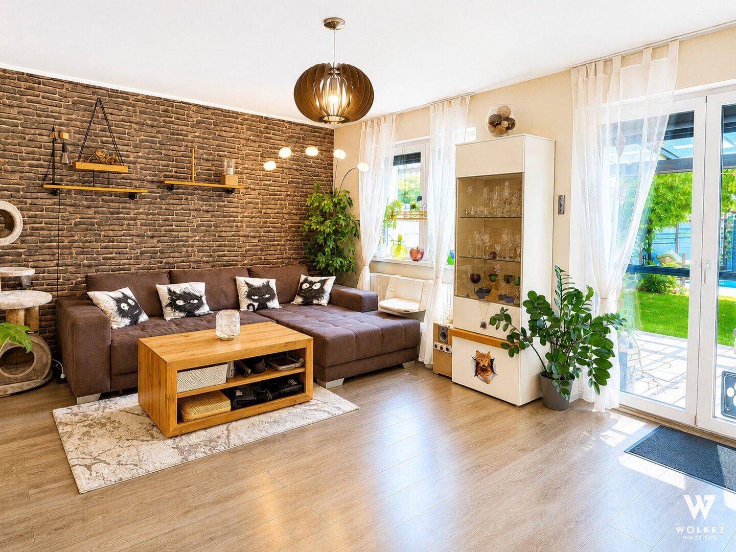 Gemütliches Wohnzimmer mit Ziegelwand, großem Sofa und Zugang zum Garten.