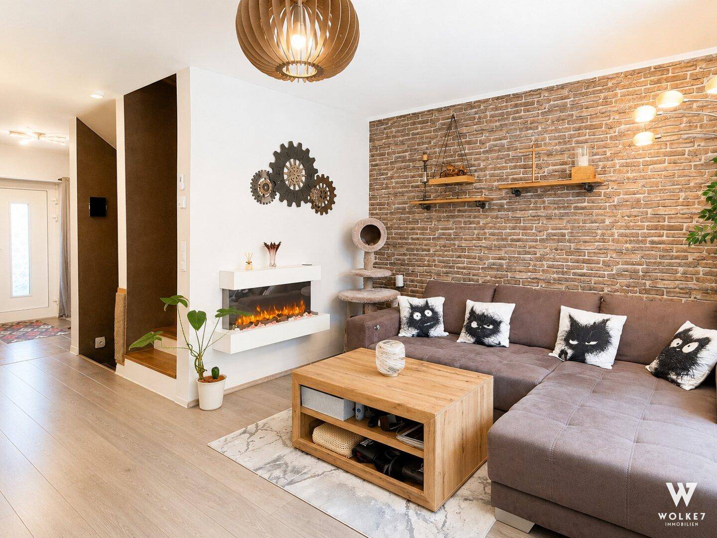 Wohnzimmer mit moderner Kaminattrappe, Ziegelwand und bequemer Sofalandschaft.