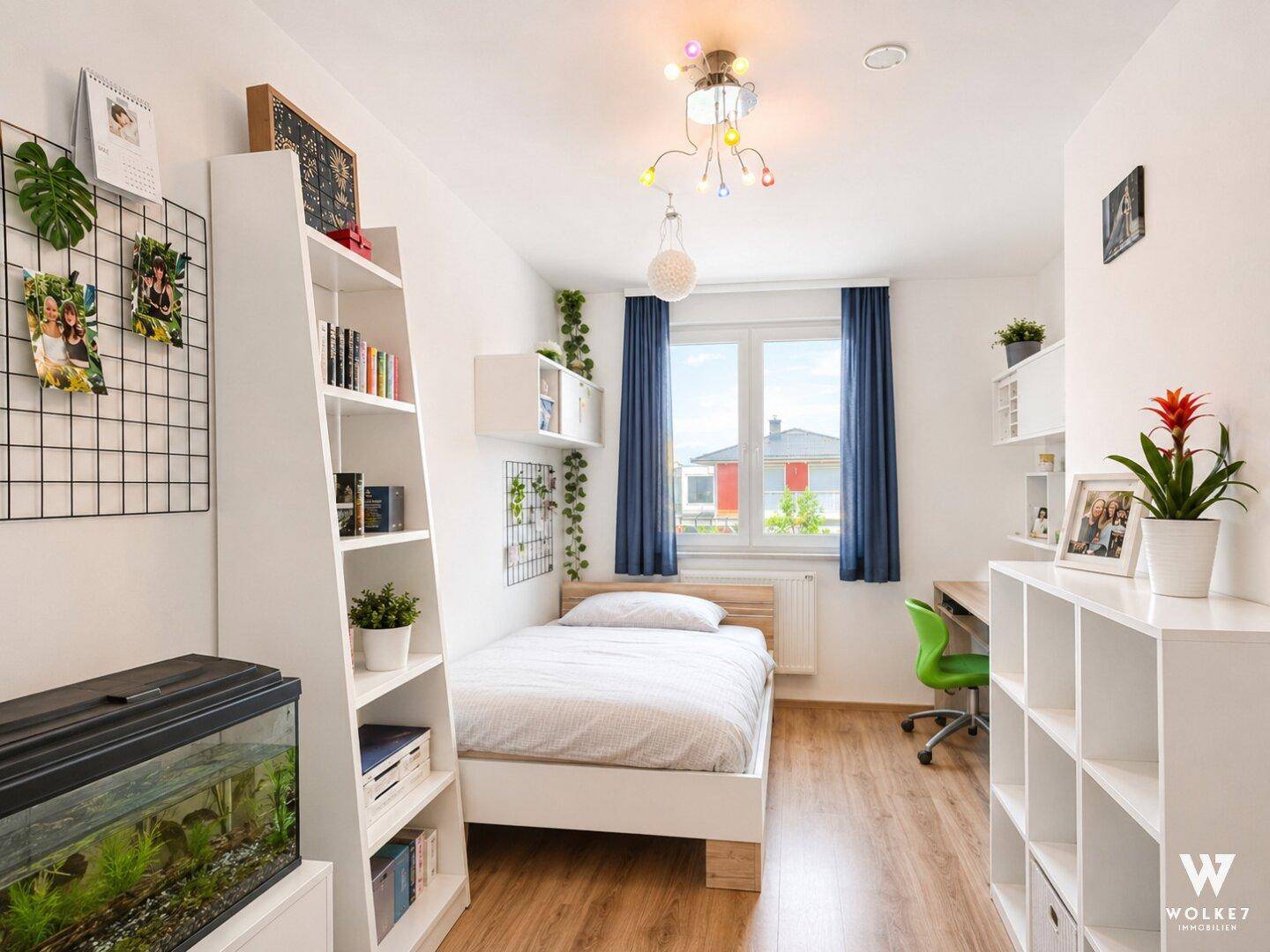 Helles Kinder- oder Gästezimmer mit Bett, Schreibtisch und Regalsystemen.