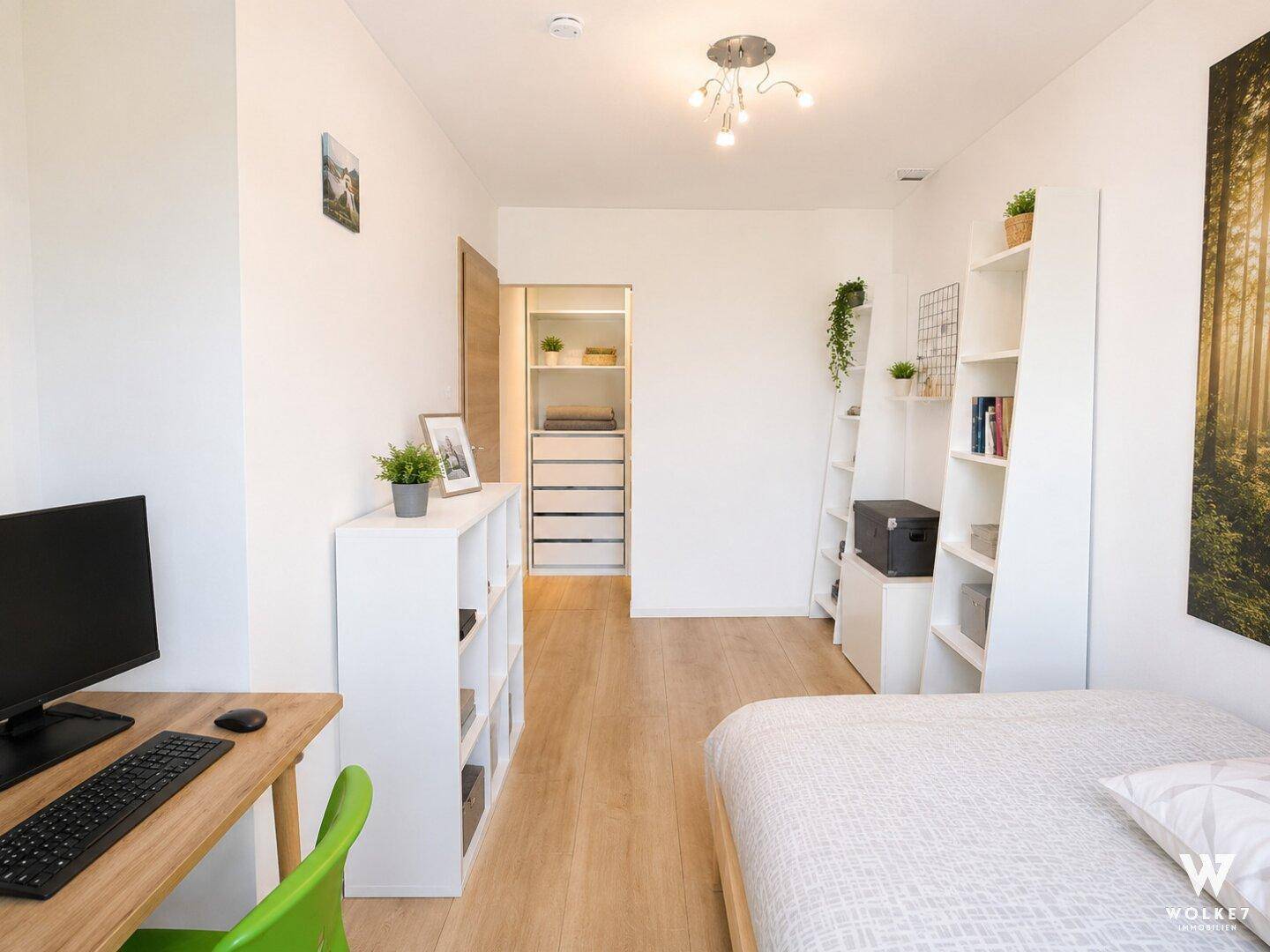 Funktionales Zimmer mit Bett, Schreibtisch und offenem Zugang zu einem Kleiderschrank.